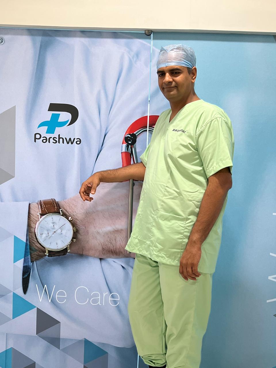 Dr. Urvish Doshi beside the Parshwa Hospital banner